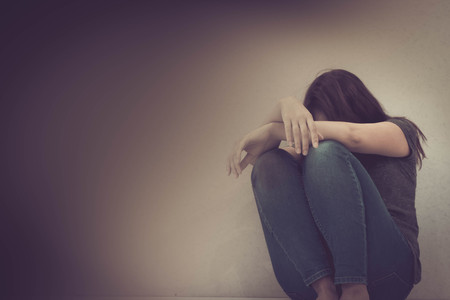 sadness young woman sitting on wood floor looking at empty dark area feeling unhappy and afraid on white wall background with battered abused woman concept.の写真素材