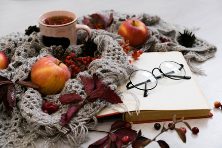 selective focus photo of grey cozy knitted scarf with cup of coffee or tea and open book on old wooden table.の写真素材