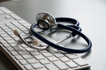 Silver stethoscope lying down on an laptop, toned blue.の写真素材