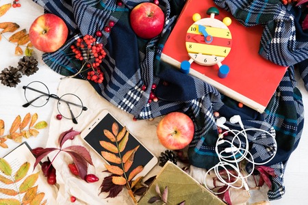 Hot coffee in mug with plaid or scarf, mobile phone with headphones, autumn leaf on a vintage table surface, selective focus.の写真素材