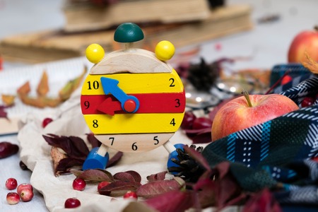 Fall Time Alarm clock on a rustic wooden table with colorful Autumn leaves. with light shadow and shallow depth of field. Daylight savings time concept. Autumn Time Change, with copy space. Top viewの写真素材
