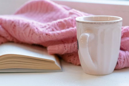 Cozy home still life: cup of hot coffee and opened book with warm plaid on windowsill against snow landscape outside. Winter holidays, Christmas time concept, free copy spaceの写真素材