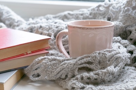 Cozy home with cup of coffee and a book. Hygge style. Mug of black coffee wrapped in warm scarf on wooden board. Top view, vintage style, Still life.の写真素材
