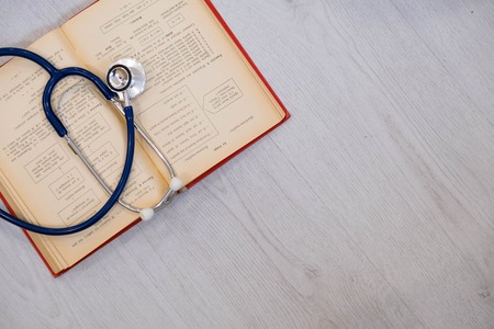 Beautiful stethoscope lying on a reference books. Stethoscope with open book on wooden background. Medical literature concept. copy space for text, selective focus Top viewの写真素材