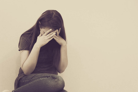 sad woman hug her knee and cry. The depression woman sit on the floor. Teenager girl with depression sitting alone on the floor in the dark room. Toned photoの写真素材