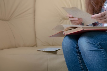 woman detail sitting on a brown sofa reading a bookの写真素材