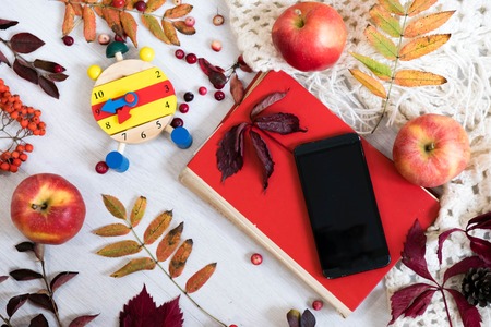 heart clock with glasses and mobile phone on red book ,education concept, mobile phone with headphones, autumn leaf on a vintage table surface, selective focusの写真素材