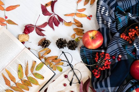 Hot coffee in mug with plaid or scarf, mobile phone with headphones, autumn leaf on a vintage table surface, selective focus.の写真素材