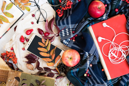 Hot coffee in mug with plaid or scarf, mobile phone with headphones, autumn leaf on a vintage table surface, selective focus.の写真素材
