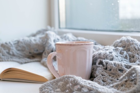 Cozy home still life: cup of hot coffee and opened book with warm plaid on windowsill against snow landscape outside. Winter holidays, Christmas time concept, free copy spaceの写真素材