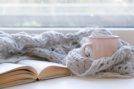 Cozy home with cup of coffee and a book. Hygge style. Mug of black coffee wrapped in warm scarf on wooden board. Top view, vintage style, Still life.の写真素材