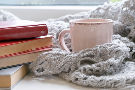Cozy home with cup of coffee and a book. Hygge style. Mug of black coffee wrapped in warm scarf on wooden board. Top view, vintage style, Still life.の写真素材