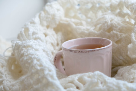 Knit cozy sweater folded in a pile on wooden background near the window . With a Cup of tea and dried lemon.Warm concept.の写真素材