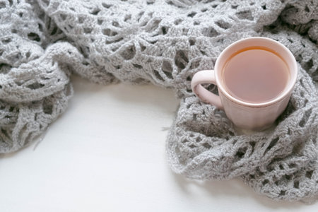 Knit cozy sweater folded in a pile on wooden background near the window . With a Cup of tea and...