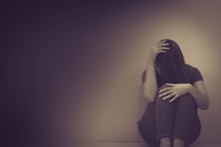 Woman holding her head in her hands, knees up, clearly upsetの写真素材