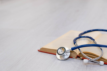 Beautiful stethoscope lying on a reference books. Stethoscope with open book on wooden background. Medical literature concept. copy space for text, selective focusの写真素材