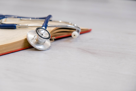 Beautiful stethoscope lying on a reference books. Stethoscope with open book on wooden background. Medical literature concept. copy space for text, selective focusの写真素材