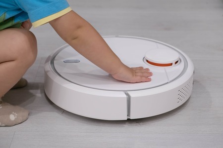 Robotic vacuum cleaner on laminate floor with baby boy on backgroundの写真素材