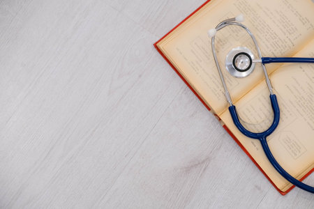 Beautiful stethoscope lying on a reference books. Stethoscope with open book on wooden background. Medical literature concept. copy space for text, selective focus Top viewの写真素材