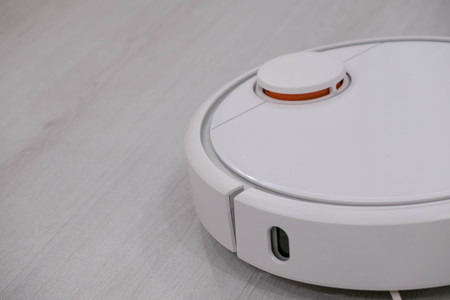 White robotic vacuum cleaner on laminate floor cleaning dust in living room interior. Smart electronic housekeeping technology.の写真素材