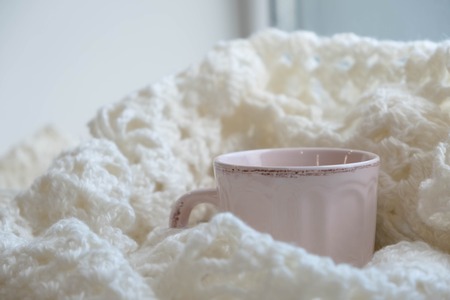 Knit cozy sweater folded in a pile on wooden background near the window . With a Cup of tea and dried lemon.Warm concept.の写真素材