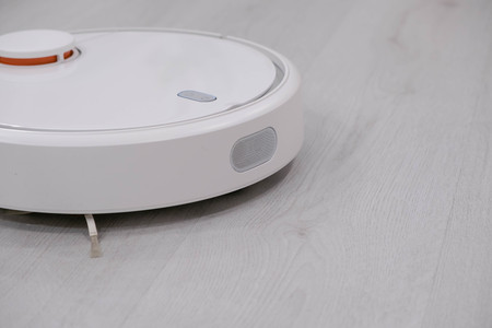 White robotic vacuum cleaner on laminate floor cleaning dust in living room interior. Smart electronic housekeeping technology.の写真素材