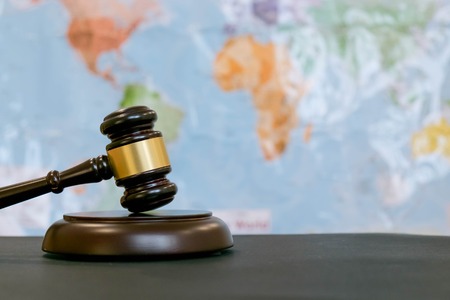 Judge's gavel and over world map. Symbol for jurisdiction. Law concept a wooden judges gavel on table in a courtroom or law enforcement office on blue background. Copy space for textの写真素材