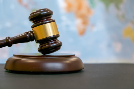 Judge's gavel and over world map. Symbol for jurisdiction. Law concept a wooden judges gavel on table in a courtroom or law enforcement office on blue background. Copy space for textの写真素材