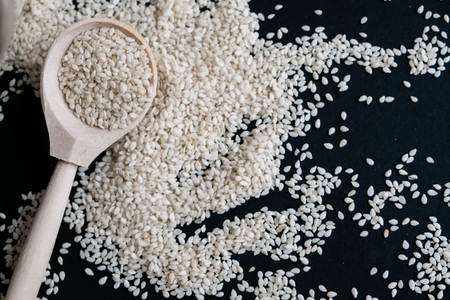 Organic natural sesame seeds wooden spoon. toasted sesame seeds. Raw, whole, unprocessed. Natural light. Selective focus. Close up on a black background. Top view, flat lay. copy space for text.の写真素材