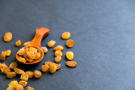 Raisins on a wooden spoon. Natural light. Selective focus. Close up on a black background. Top view, flat lay. copy spaceの写真素材