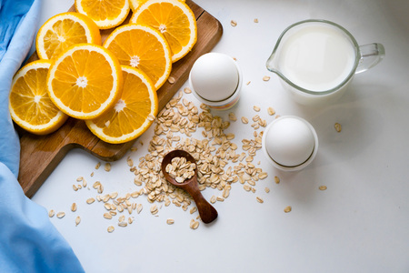 Oat flakes plate with milk, orange, eggs on a wooden white table. Top view of healthy oat flakes breakfast. Copy spaceの写真素材