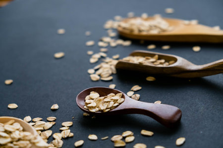 Oat stems and oat flakes in a wooden spoon on a dark background. Natural light. Selective focus....