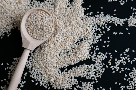 Organic natural sesame seeds wooden spoon. toasted sesame seeds. Raw, whole, unprocessed. Natural light. Selective focus. Close up on a black background. Top view, flat lay. copy space for text.の写真素材