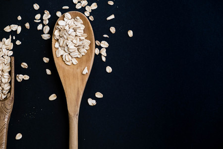 Oat stems and oat flakes in a wooden spoon on a dark background. Natural light. Selective focus. Close up on a black background. Top view, flat lay. copy space. dried grapes.の写真素材