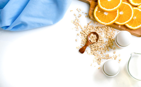 Oat flakes plate with milk, orange, eggs on a wooden white table. Top view of healthy oat flakes breakfast. Copy space. blue napkin Breakfast in bed plate, breakfast table buffet. Healthy ingredientsの写真素材