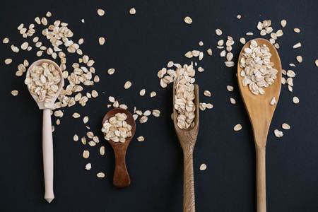 Oat stems and oat flakes in a wooden spoon on a dark background. Natural light. Selective focus. Close up on a black background. Top view, flat lay. copy space. dried grapes.の写真素材