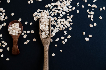 Oat stems and oat flakes in a wooden spoon on a dark background. Natural light. Selective focus. Close up on a black background. Top view, flat lay. copy space. dried grapes.の写真素材