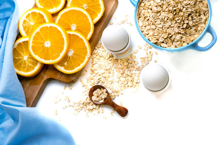 Oat flakes plate with milk, orange, eggs on a wooden white table. Top view of healthy oat flakes breakfast. Copy space. blue napkin Breakfast in bed plate, breakfast table buffet. Healthy ingredientsの写真素材