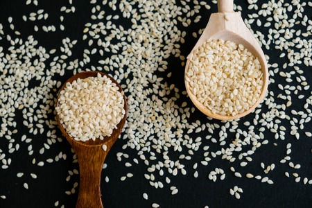 Organic natural sesame seeds wooden spoon. toasted sesame seeds. Raw, whole, unprocessed. Natural light. Selective focus. Close up on a black background. Top view, flat lay. copy space for text.の写真素材
