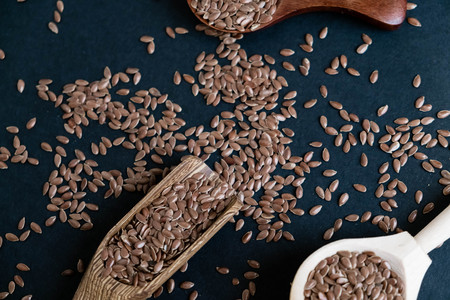 Flax seeds in spoons over dark background. Natural light. Selective focus. Close up on a black background. Top view, flat lay. copy spaceの写真素材