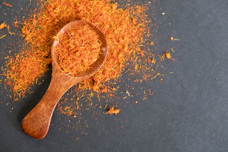 Dried saffron spice on black background. Raw Organic pistil powder saffron are scattered on the table. Red Saffron Spice in a wooden spoon on black backgroundの写真素材