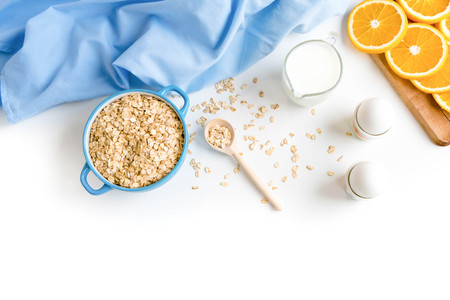 Oat flakes plate with milk, orange, eggs on a wooden white table. Top view of healthy oat flakes breakfast. Copy space. blue napkin Breakfast in bed plate, breakfast table buffet. Healthy ingredientsの写真素材