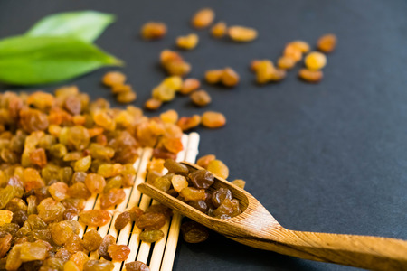 Raisins on a wooden spoon. Natural light. Selective focus. Close up on a black background. Top view, flat lay. copy spaceの写真素材