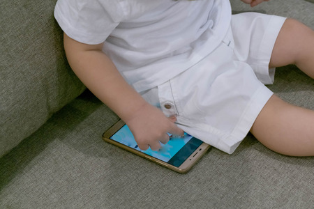 Adorable toddler boy sitting on the sofa in the living room and playing with smartphone. Child learning how to use smartphone. Boy texting on the phone. - technology and lifestyle conceptの写真素材