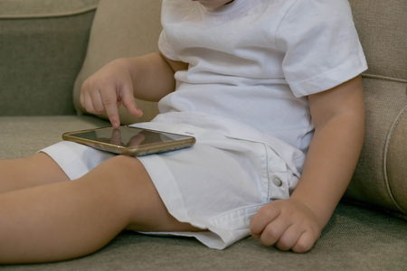 Adorable toddler boy sitting on the sofa in the living room and playing with smartphone. Child learning how to use smartphone. Boy texting on the phone. - technology and lifestyle conceptの写真素材
