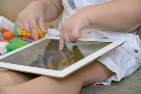 Toddler boy playing with digital tablet on couch at homeの写真素材