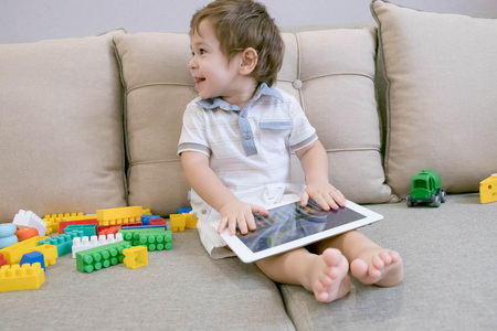 Toddler boy playing with digital tablet on couch at homeの写真素材