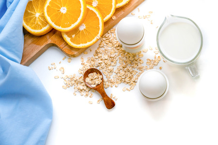 Oat flakes plate with milk, orange, eggs on a wooden white table. Top view of healthy oat flakes breakfast. Copy space. blue napkin Breakfast in bed plate, breakfast table buffet. Healthy ingredients.の写真素材