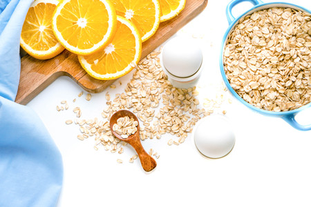Oat flakes plate with milk, orange, eggs on a wooden white table.の写真素材