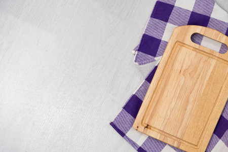 Cutting board over towel on wooden kitchen table. Kitchen purple plaid color kitchen cloth. Food...
